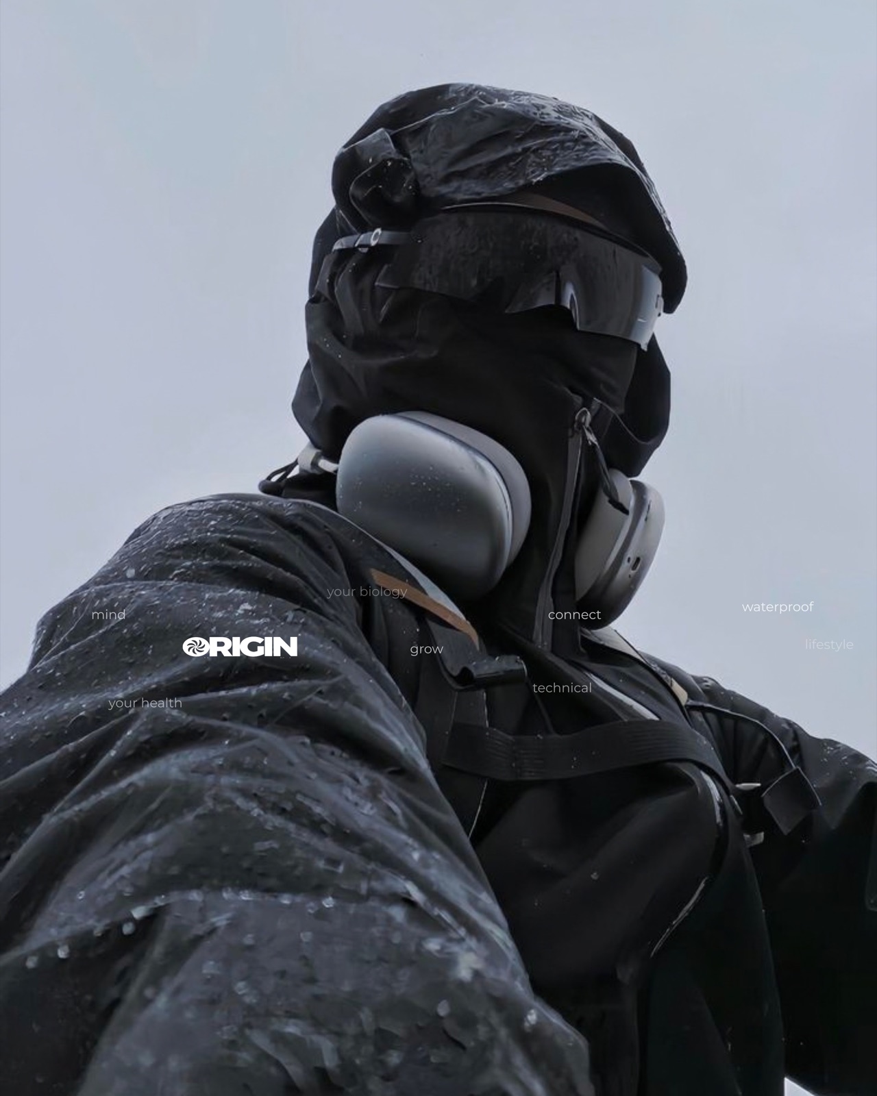 Persona con chaqueta impermeable negra bajo la lluvia, con el logo de Origin y las palabras mind, grow, connect