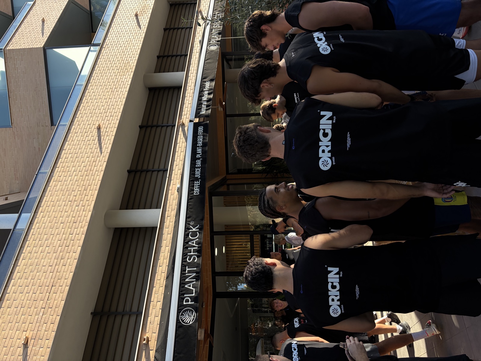 Miembros de Origin de espaldas con sus camisetas frente a Plant Shack