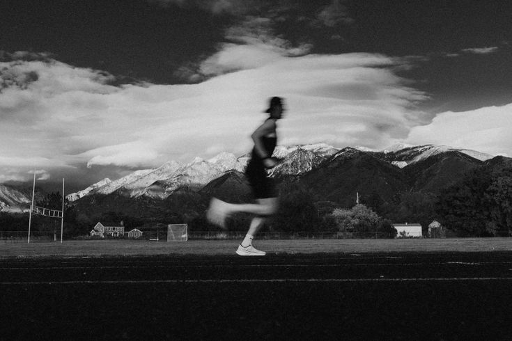 Persona corriendo en una pista frente a montañas nevadas, en blanco y negro